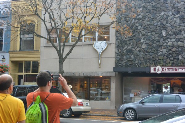 A Dali-esque clock suspended from a second story window.